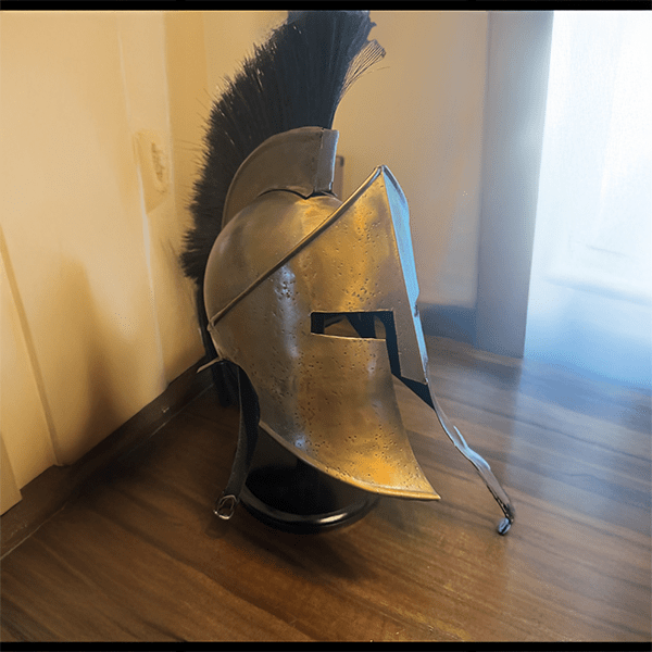 A bronze Corinthian helmet with a black plume sits on a wooden surface. The helmet, with a weathered texture, evokes a sense of ancient warrior strength.